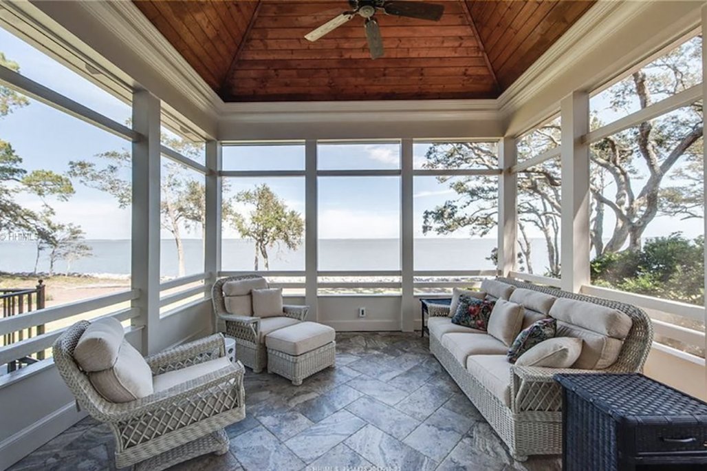 Screened porch with a wood ceiling and stone tile floor overlooking the water by Burson Construction, Bluffton SC